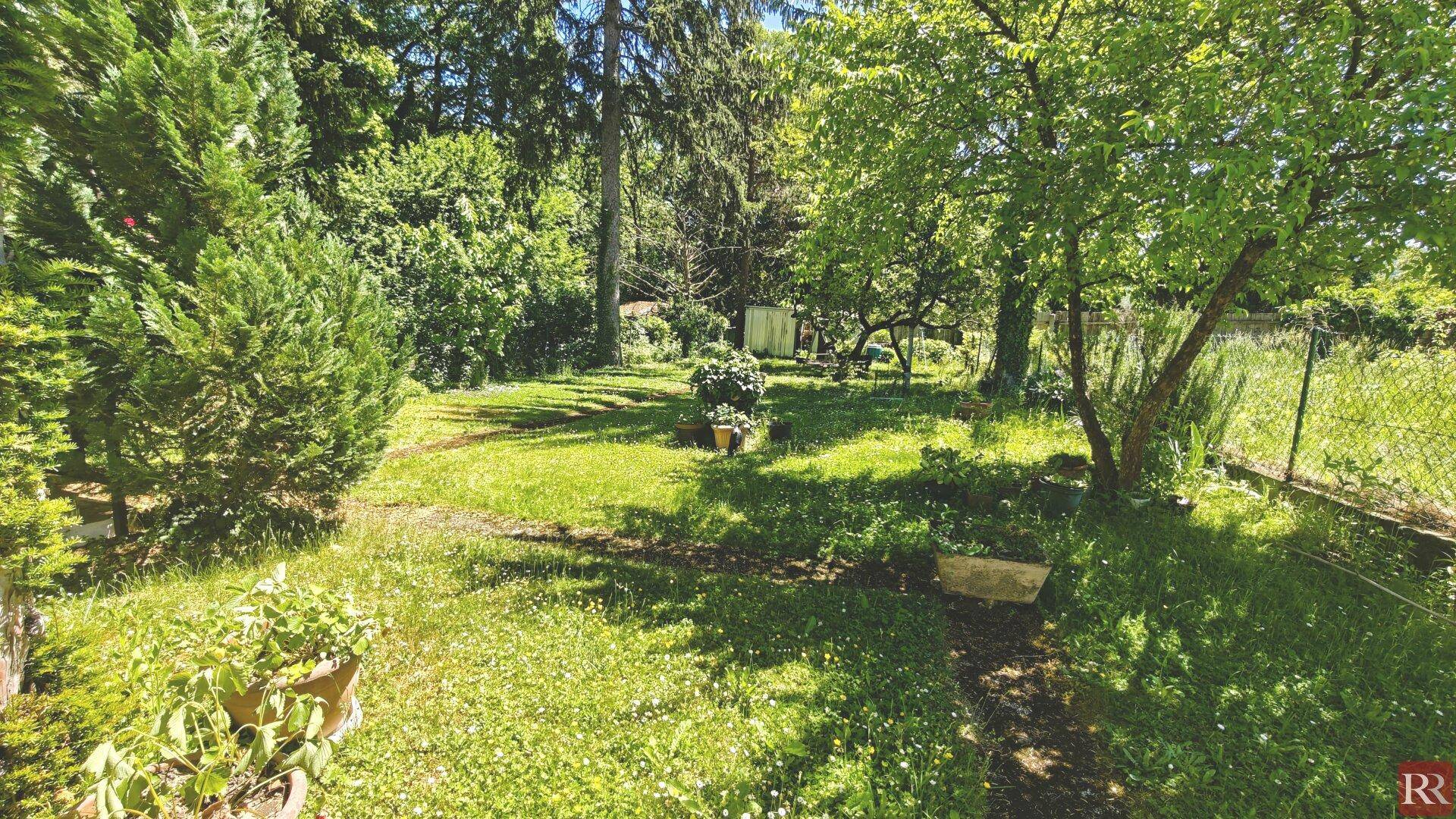Weitläufiger Gartenbereich mit üppiger Vegetation, Bäumen und einem Pfad durch das Gras.