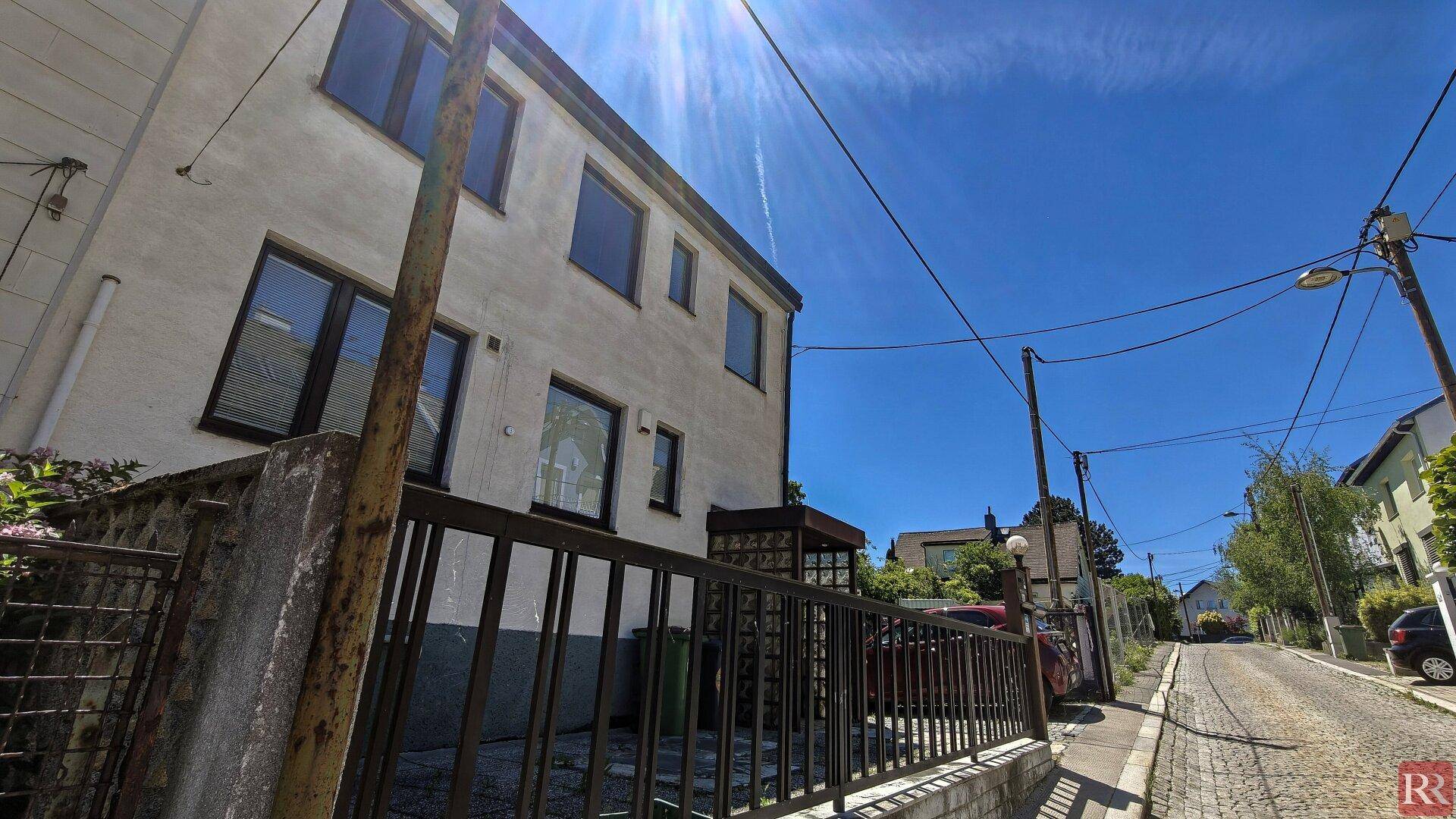 Ansicht der Hausfassade von der Straße aus mit einem Zaun im Vordergrund und klarem Himmel.
