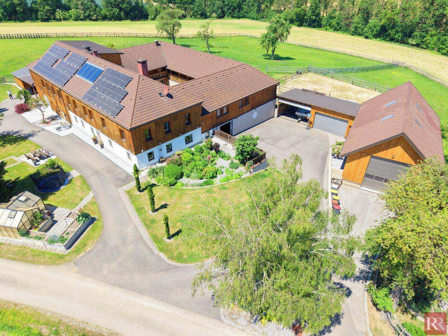 Luftaufnahme eines weitläufigen Anwesens mit mehreren Gebäuden, Solaranlagen und gepflegten Gärten.