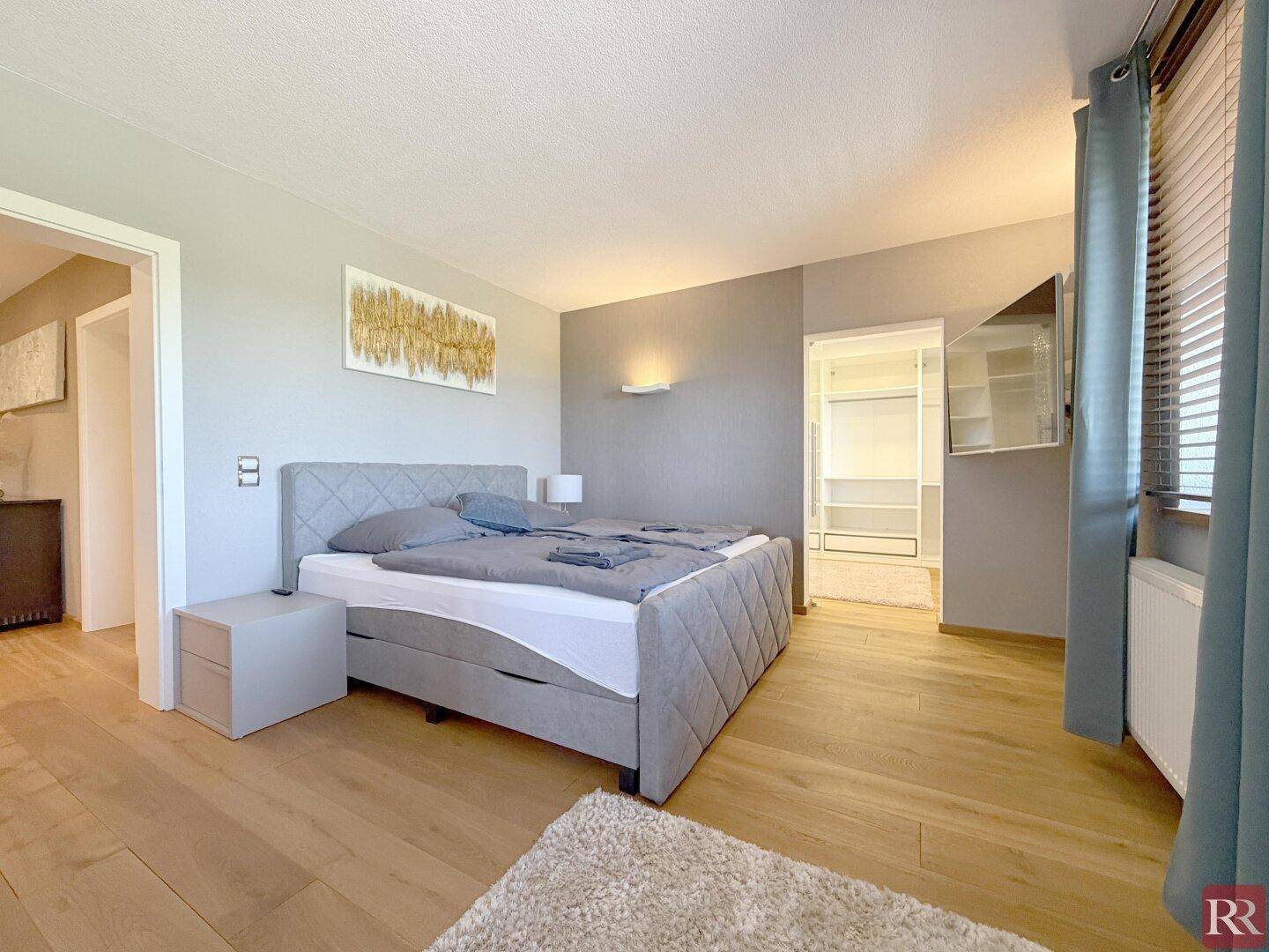 Modernes Schlafzimmer mit Doppelbett, Holzboden und integriertem begehbarem Kleiderschrank.