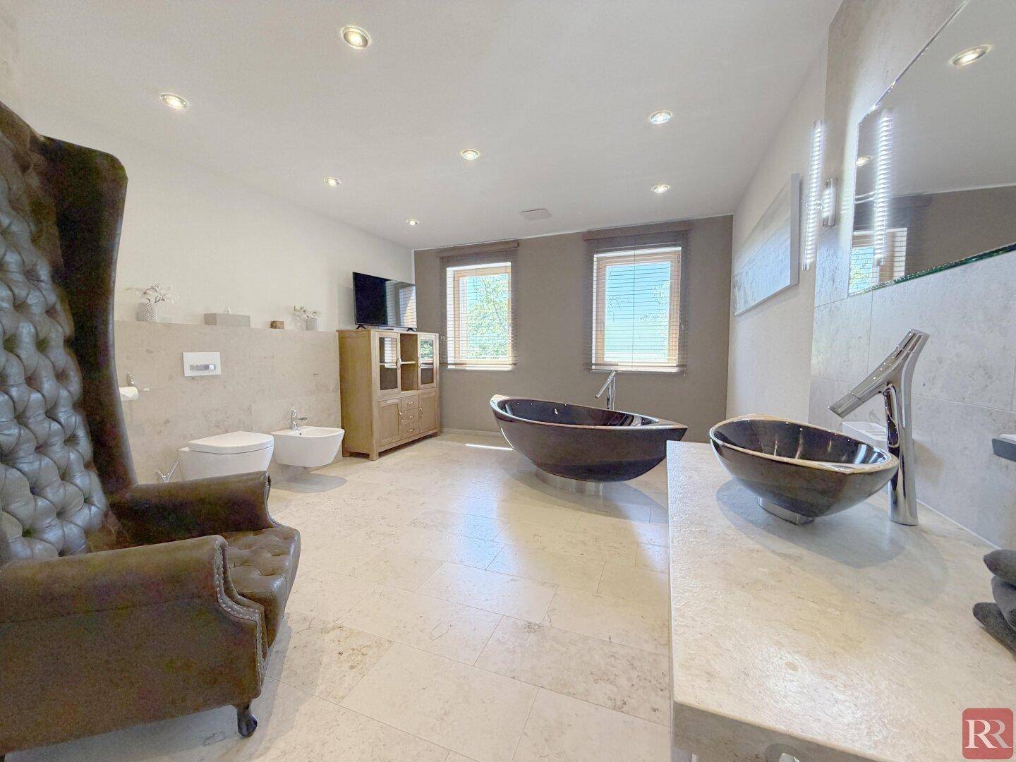 Geräumiges Badezimmer mit freistehender Badewanne, Doppelwaschbecken und separatem WC-Bereich.