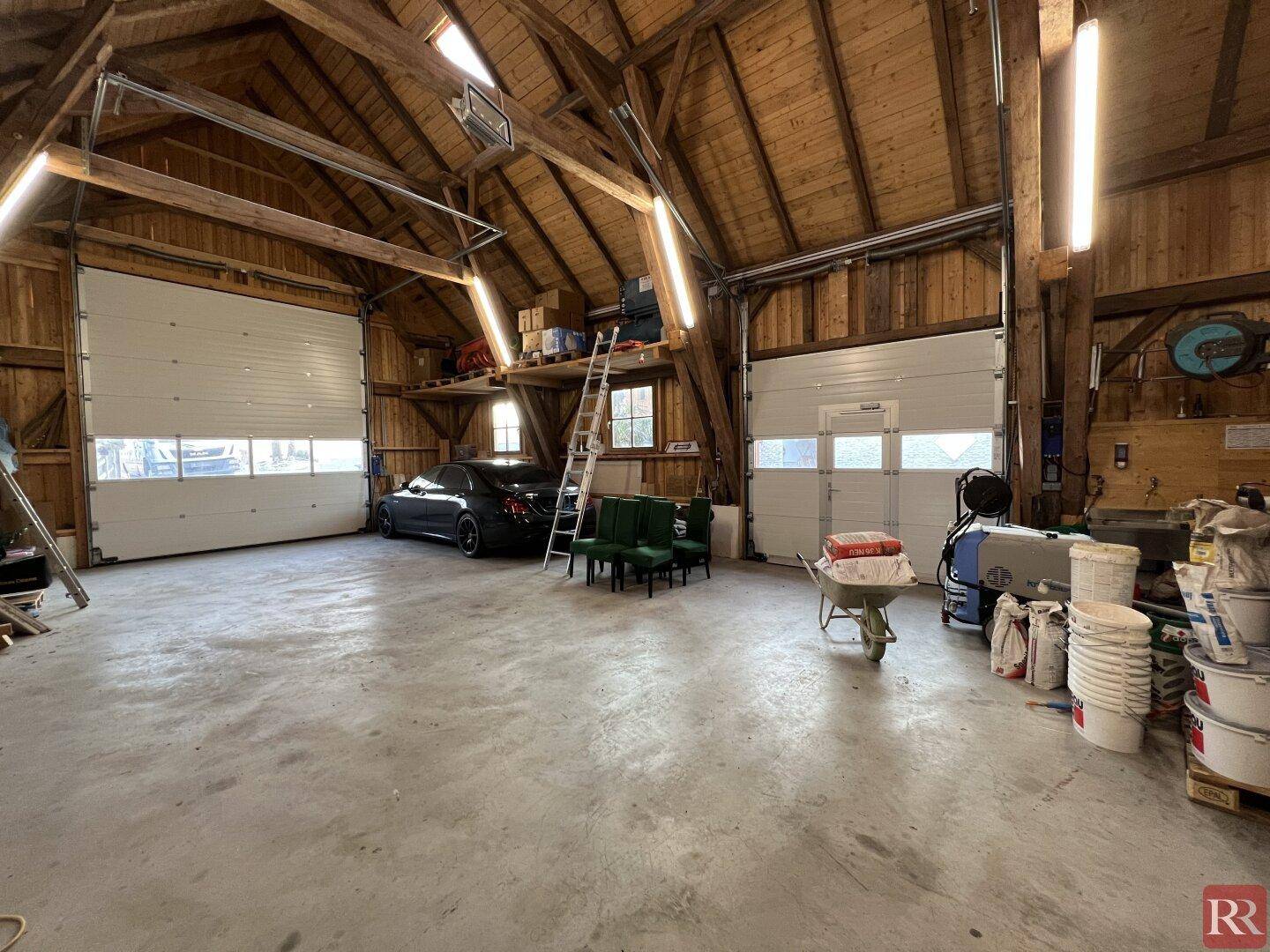 Geräumige Garage mit hohen Decken, Holzbalken und Platz für mehrere Fahrzeuge und Lagerung.