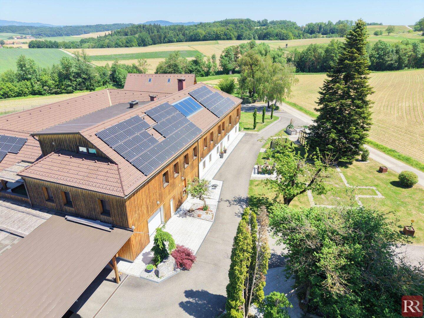 Luftaufnahme des weitläufigen Anwesens mit Solaranlagen auf dem Dach und umgebender Naturlandschaft.