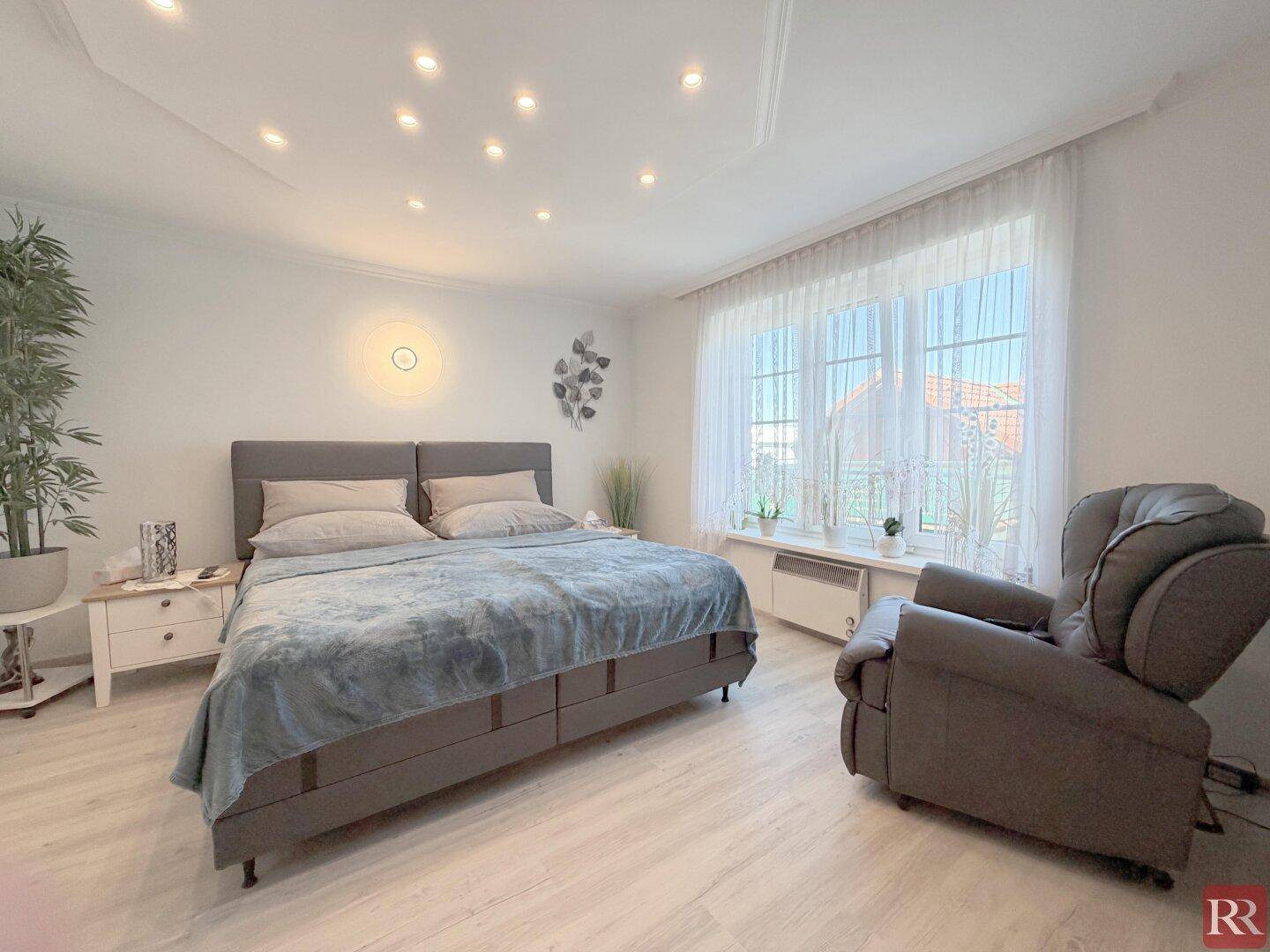 Helles Schlafzimmer mit großem Bett, modernem Laminatboden und vielen Deckenleuchten.