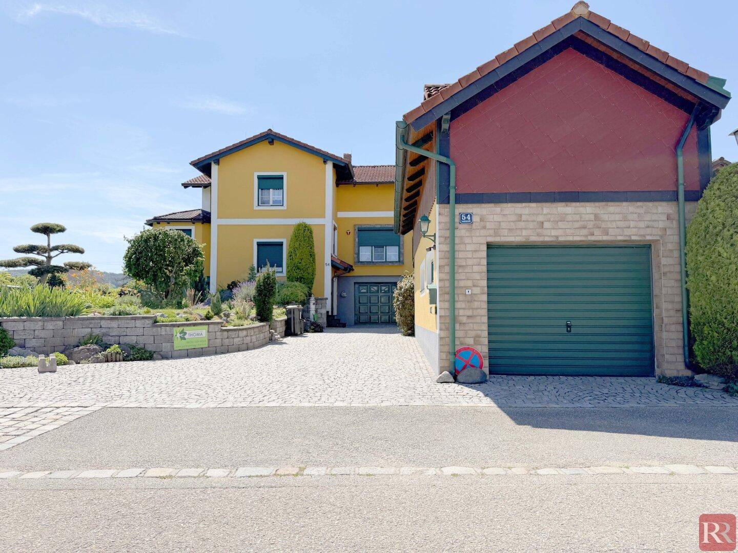 Vorderansicht des Hauses mit Garage, gepflasterter Einfahrt und gepflegtem Vorgarten.