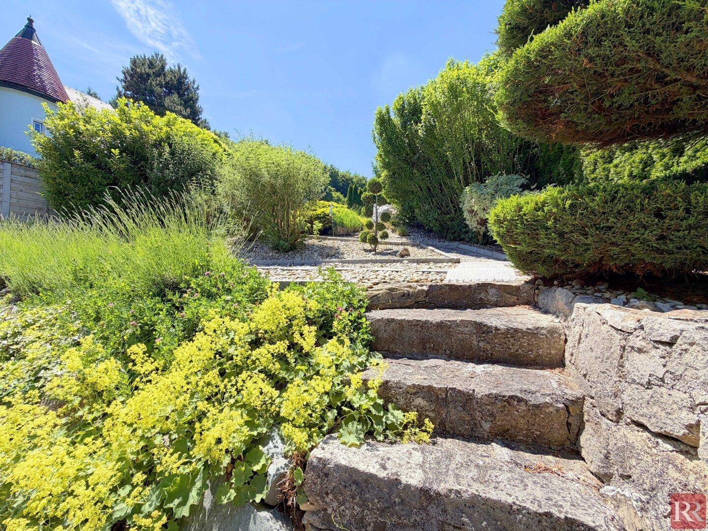 Gepflegter Garten mit Natursteintreppe, üppiger Bepflanzung und sonnigen Bereichen.