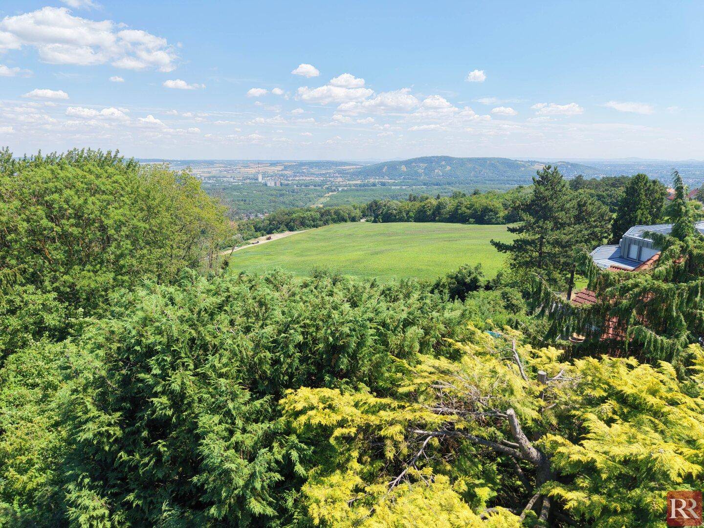 Weitläufiger Panoramablick über grüne Felder und Hügel, mit einem Teil der Wohnbebauung sichtbar.