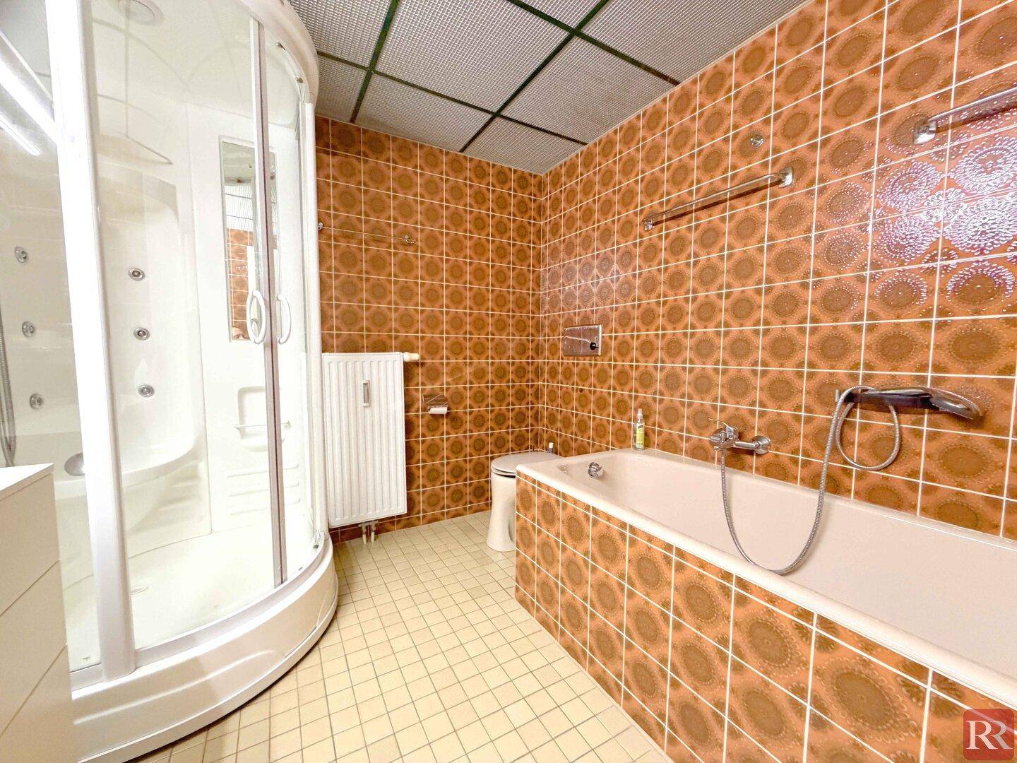 Badezimmer mit braunen Fliesen, Badewanne, Toilette und einer Duschkabine.