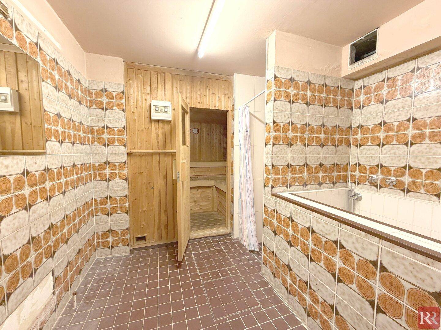 Badezimmer mit gemusterten Fliesen, Badewanne und integrierter Sauna.