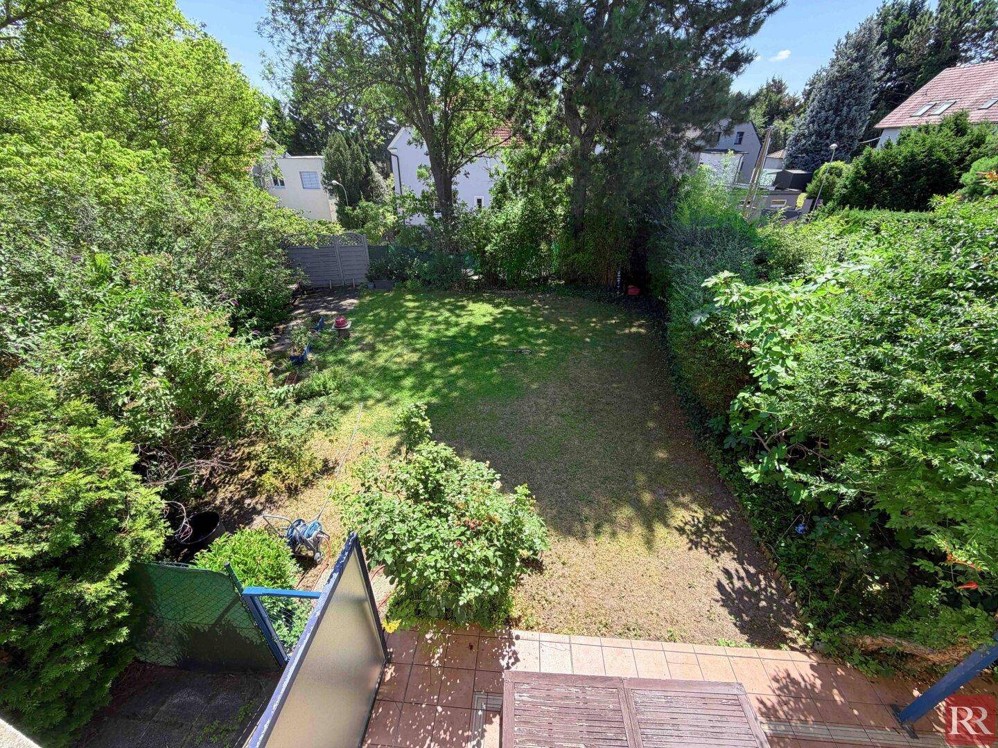 Blick von oben auf den grünen Garten mit Rasenfläche, umgeben von Hecken und Bäumen.