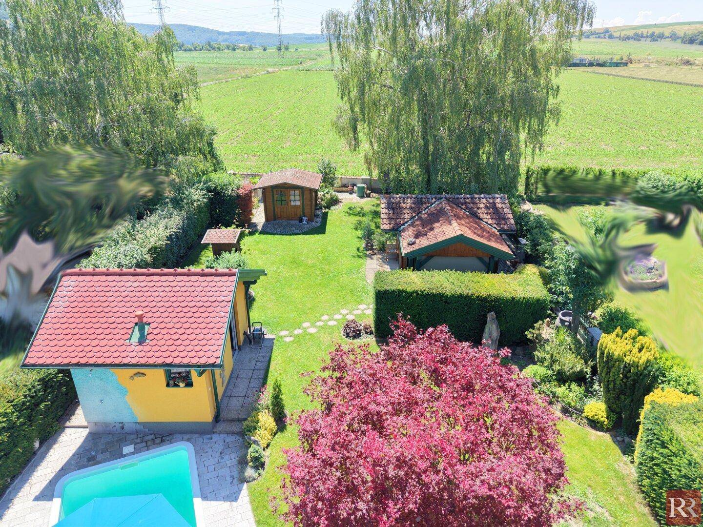 Weitläufiger Gartenbereich mit mehreren Gartenhäusern, Pool und Blick auf die umliegende Landschaft.