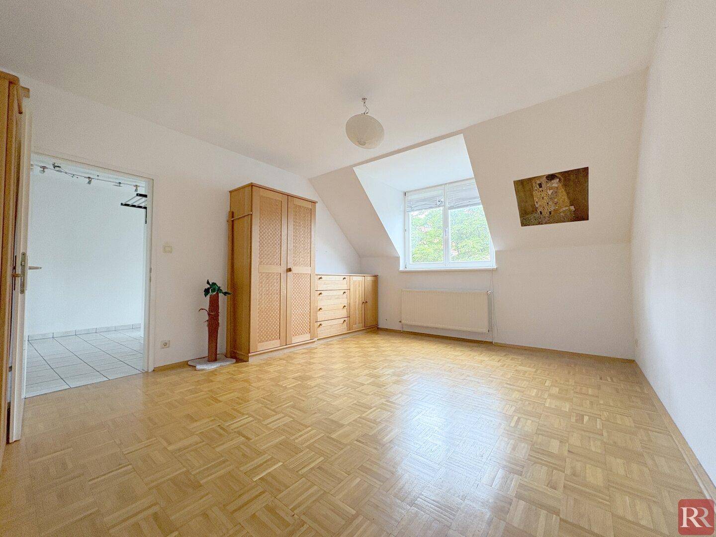 Helles Schlafzimmer mit Parkettboden, Holzmöbeln und einem Fenster in der Dachschräge, das viel Licht spendet.