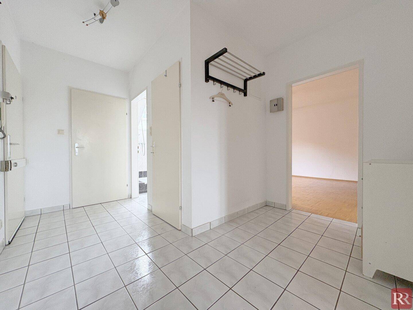 Heller Eingangsbereich mit weißen Fliesen, praktischer Garderobe und Zugang zu weiteren Räumen der Wohnung.