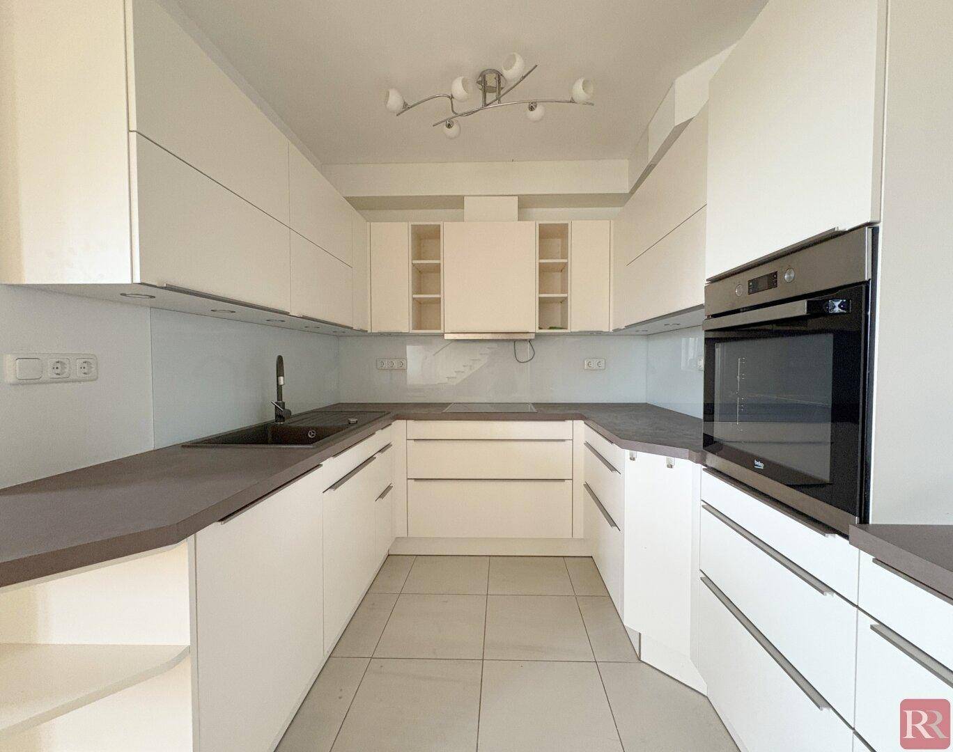 Moderne Küche mit weißen Schränken, grauen Arbeitsplatten und integriertem Backofen, ideal für kulinarische Aktivitäten.