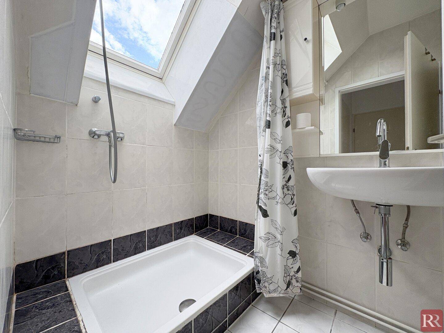 Funktionales Badezimmer mit Dusche, Waschbecken, Spiegelschrank und einem Dachfenster für natürliches Licht.