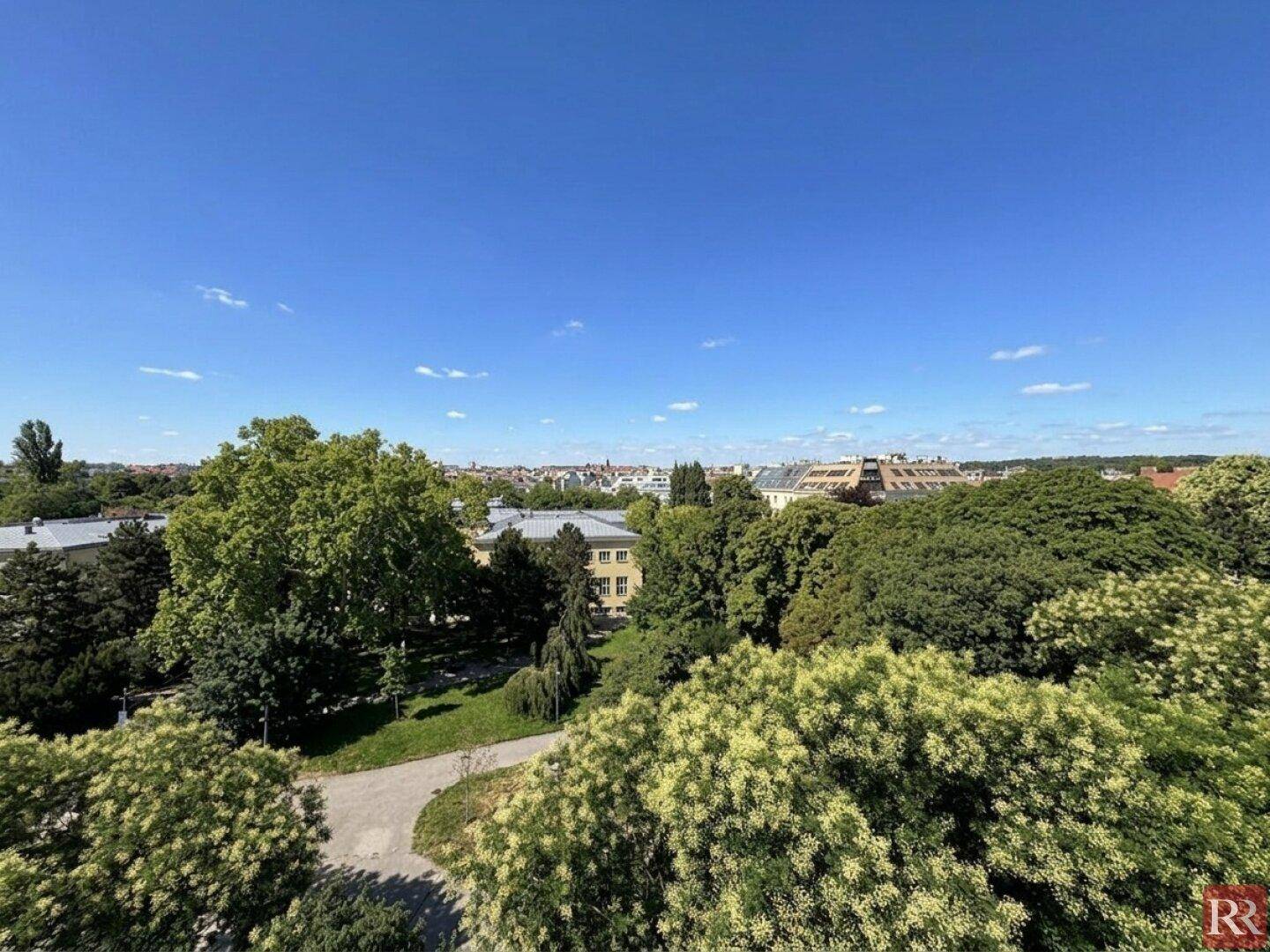 Weitläufiger Blick über die Stadt mit zahlreichen grünen Bäumen unter einem strahlend blauen Himmel.