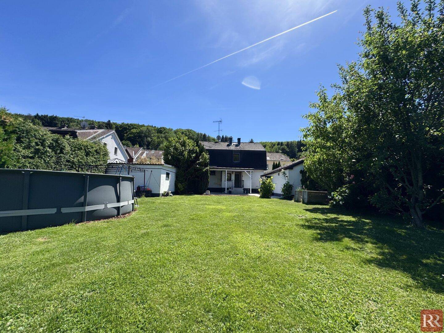 Weitläufiger Garten mit Rasenfläche und Aufstellpool, Blick auf das Haus und die umliegende Natur.