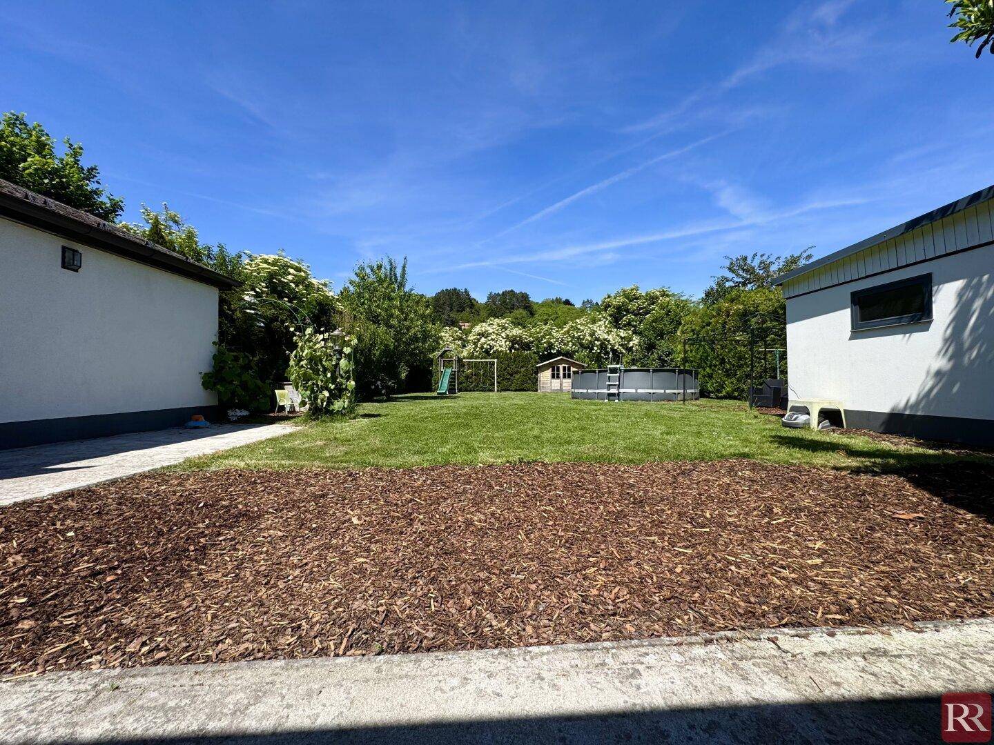 Gepflegter Gartenbereich mit Rasen, Spielplatz, Pool und Gartenhaus, umgeben von Nebengebäuden.