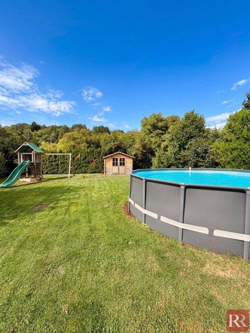 Lebendiger Garten mit gefülltem Aufstellpool, Kinderspielplatz und Gartenhaus unter strahlend blauem Himmel.