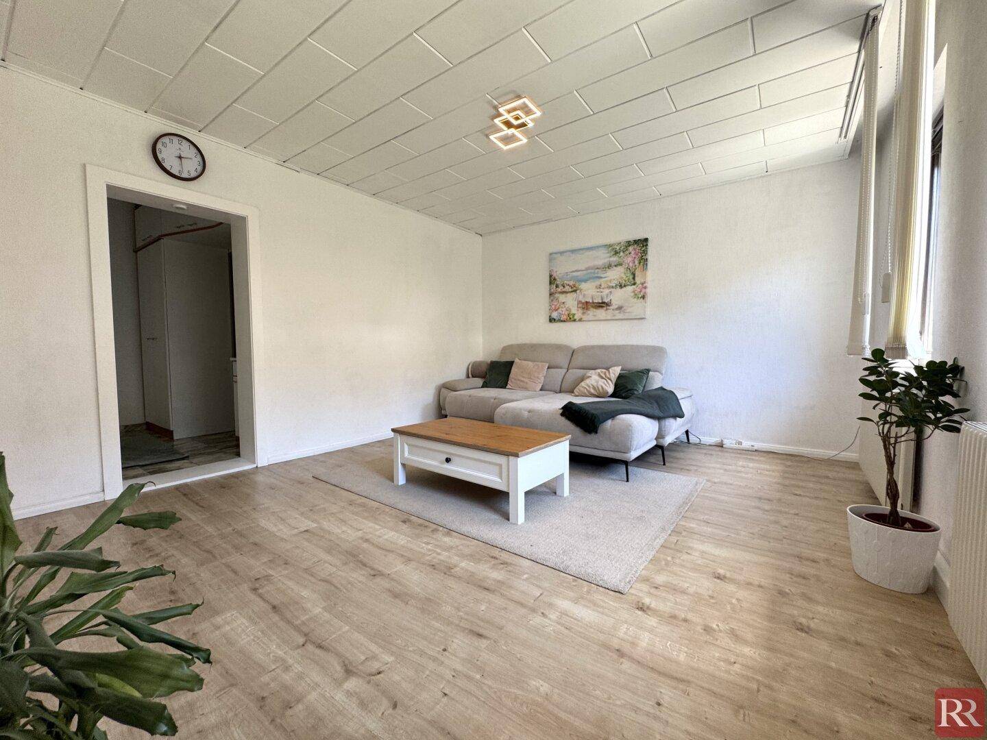 Helles Wohnzimmer mit Laminatboden, bequemer Couch und modernem Couchtisch.