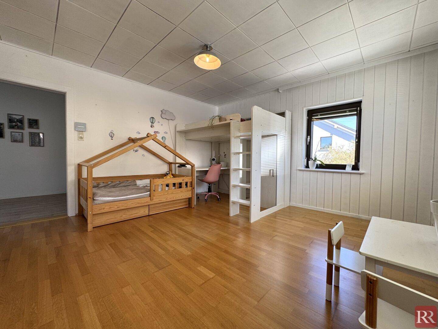 Helles Kinderzimmer mit Holzboden, kreativen Betten und Schreibtisch am Fenster.