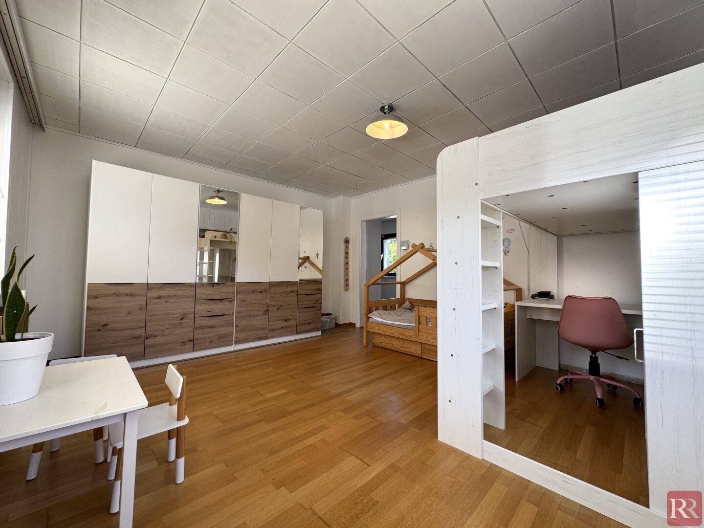 Geräumiges Kinderzimmer mit großem Kleiderschrank, Holzboden und Spielbereich.