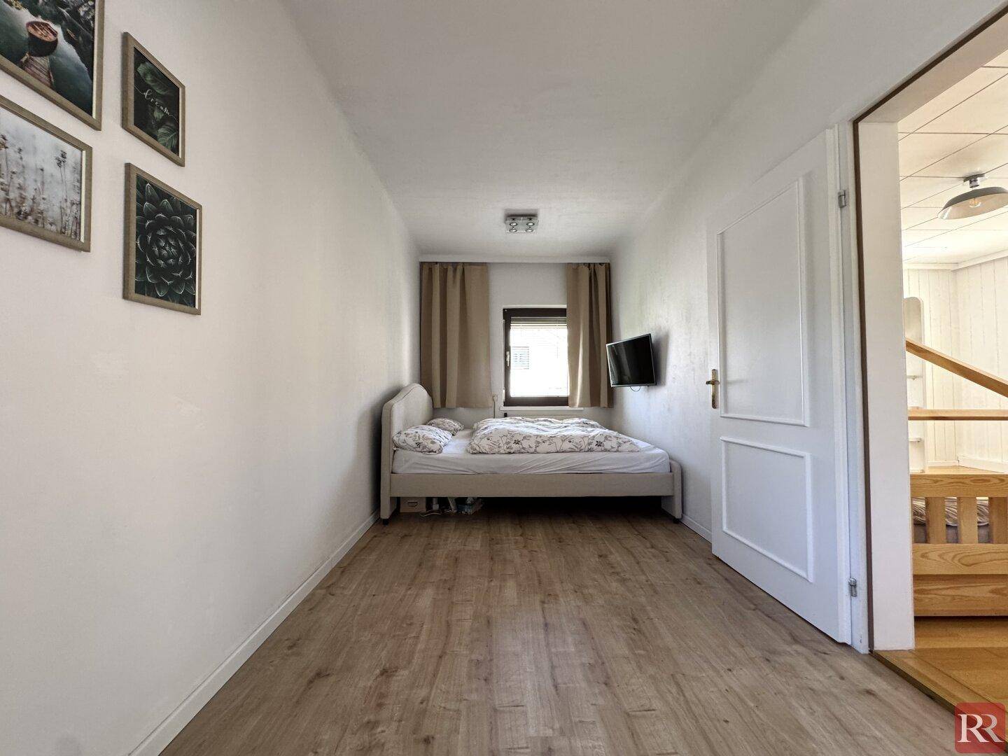Schlichtes Schlafzimmer mit Bett, Fenster und Wandfernseher, ideal für Gäste.