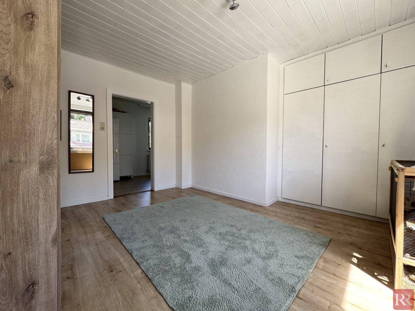 Heller Raum mit Laminatboden, Teppich und großem Einbauschrank.