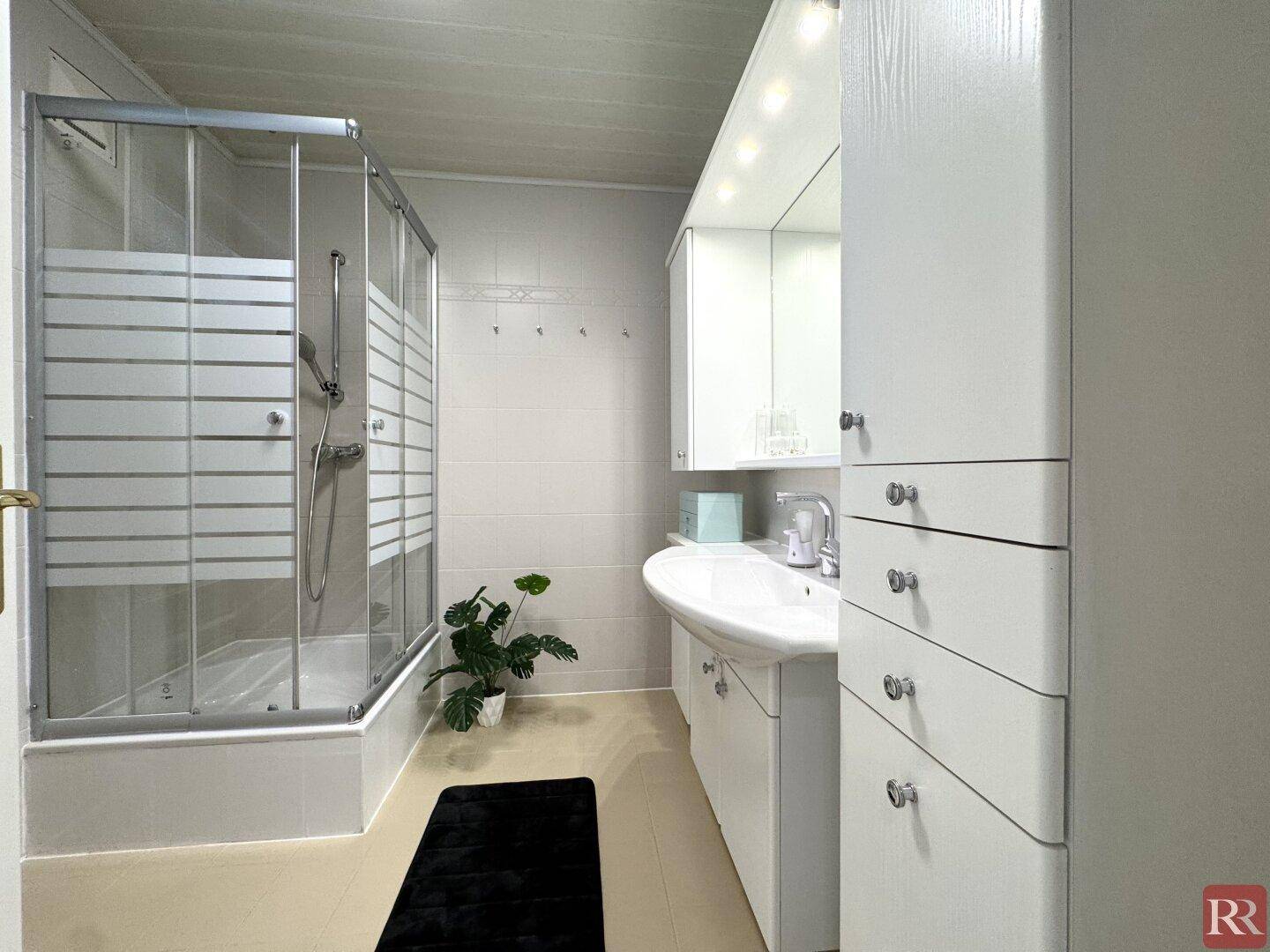 Modernes Badezimmer mit Duschkabine, Waschtisch und viel Stauraum.