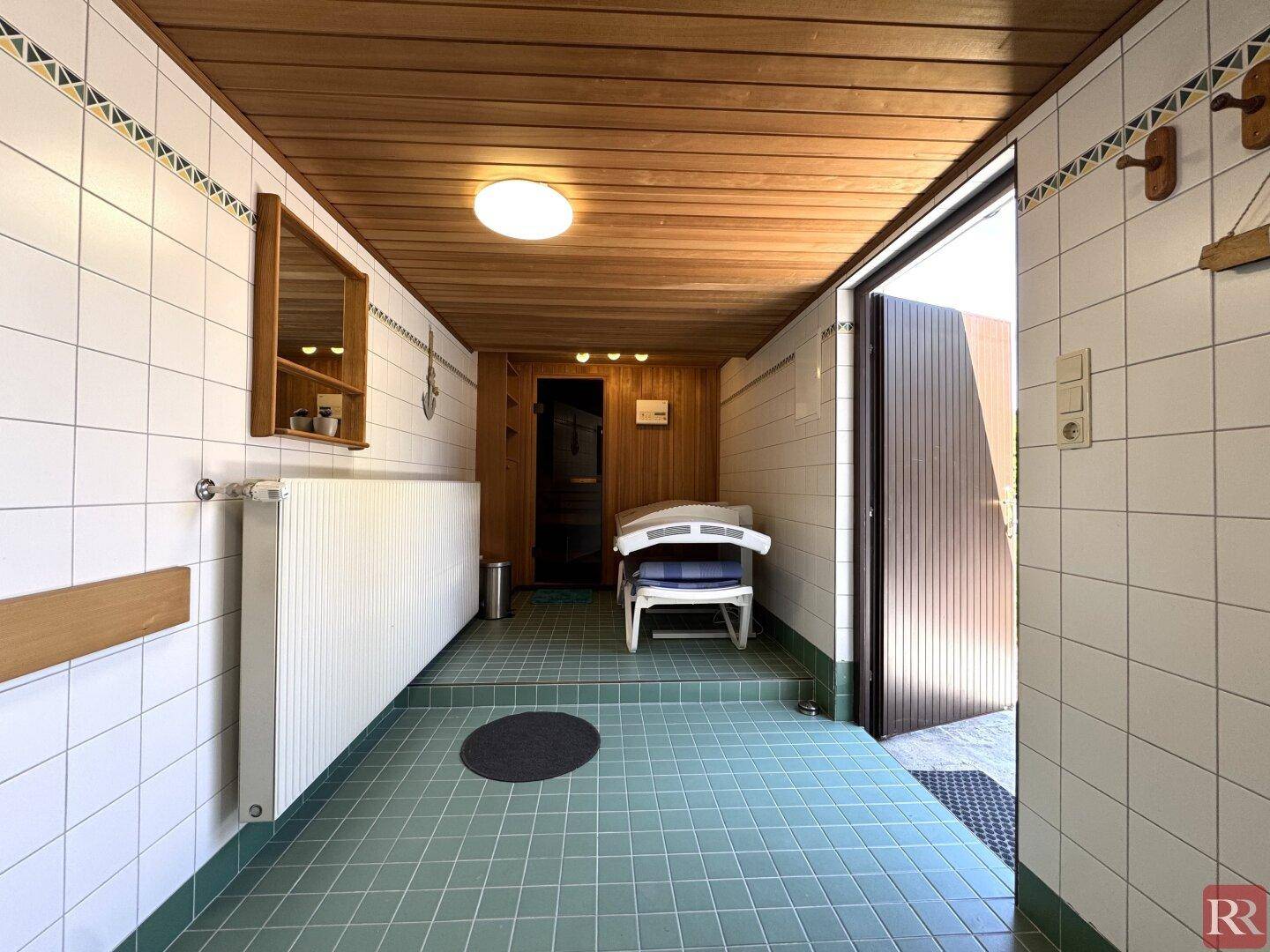Gefliester Vorraum mit Zugang zur Sauna, ausgestattet mit Heizkörper und Sitzgelegenheit.