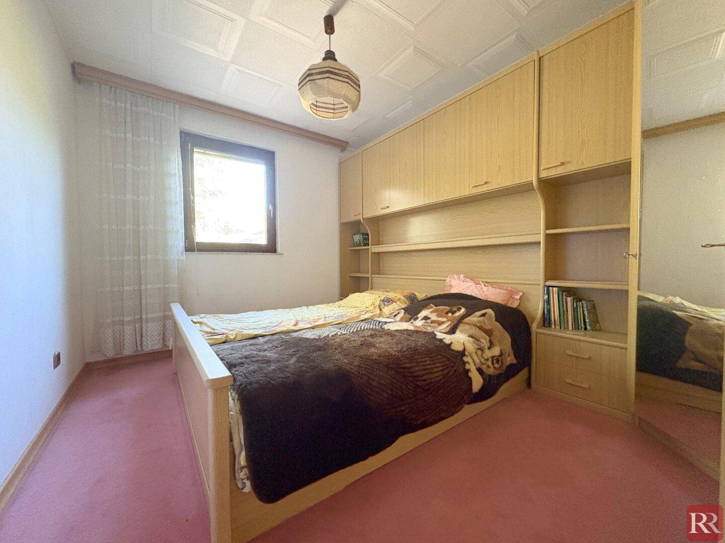Schlafzimmer mit rosa Teppichboden, Einbauschränken und einem Fenster.