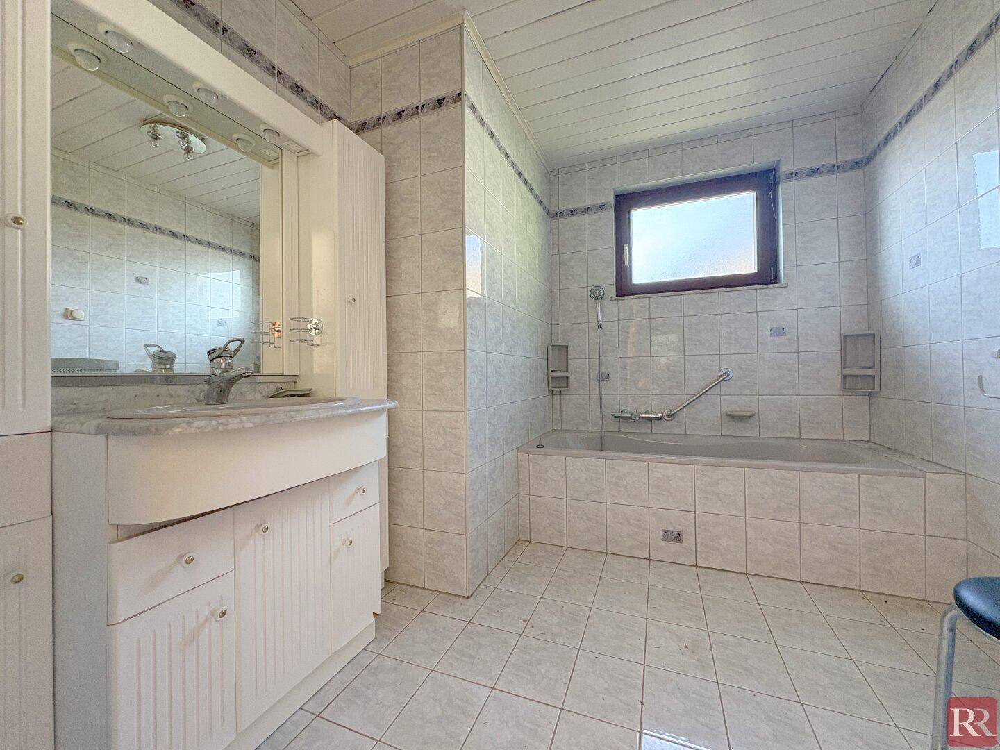 Gefliestes Badezimmer mit Badewanne, Einzelwaschbecken und Fenster.