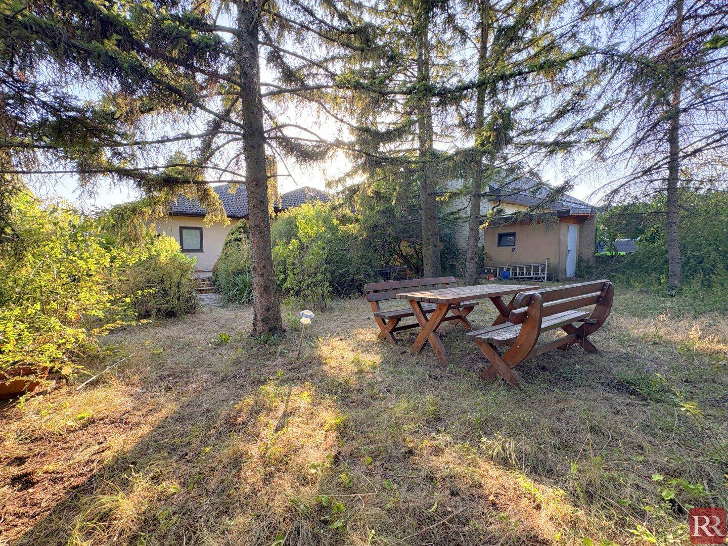 Großer Garten mit Rasenfläche, Bäumen und einem Holztisch mit Bänken.