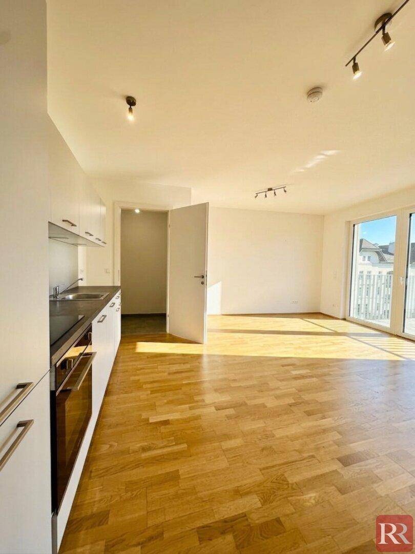 Offener Wohnbereich mit moderner Küche und Zugang zum Balkon, durchflutet von natürlichem Sonnenlicht.