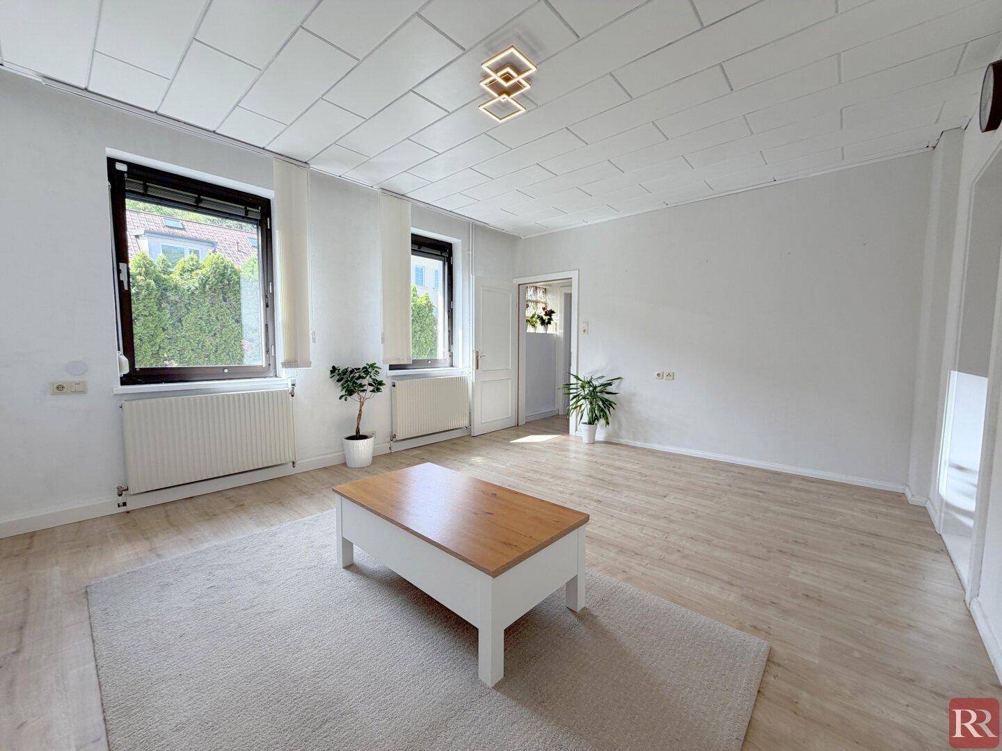 Helles Wohnzimmer mit Laminatboden, Couchtisch und großen Fenstern mit Blick ins Grüne.