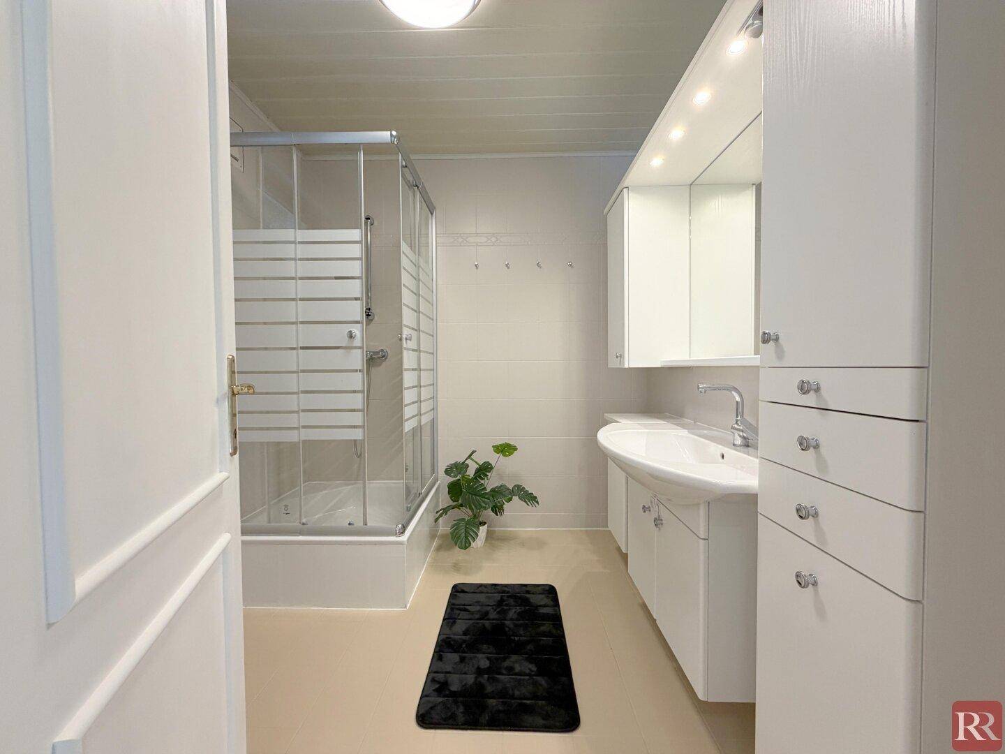 Modernes Badezimmer mit Duschkabine, Einzelwaschbecken und weißen Schränken.