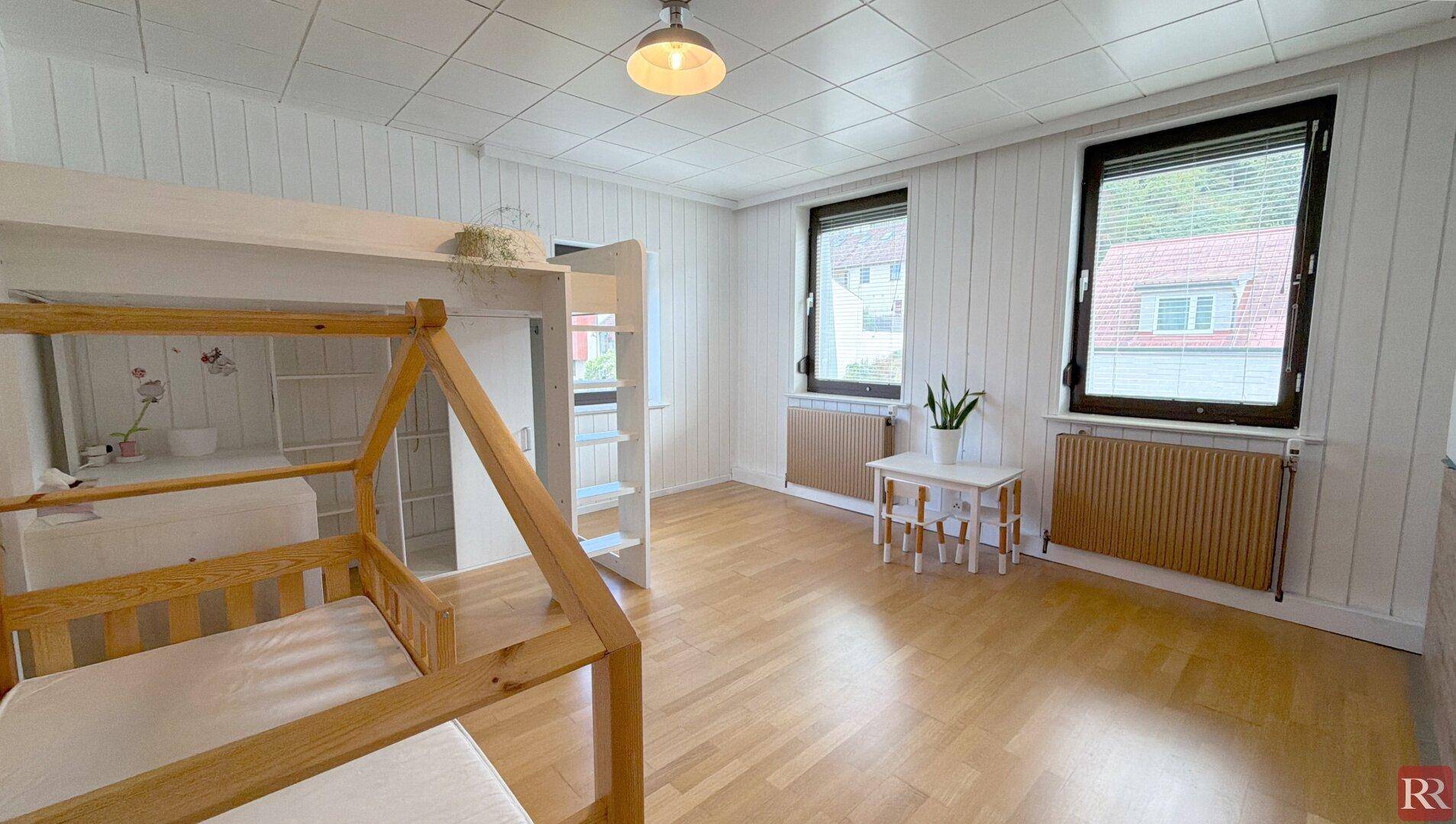 Kinderzimmer mit Etagenbett, Holzvertäfelung und zwei Fenstern für viel Tageslicht.