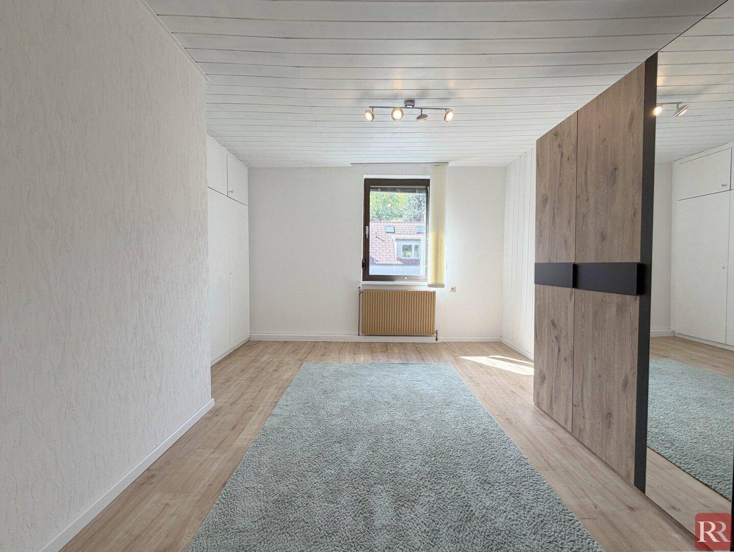 Geräumiges Schlafzimmer mit Laminatboden, großem Teppich und Einbauschränken.