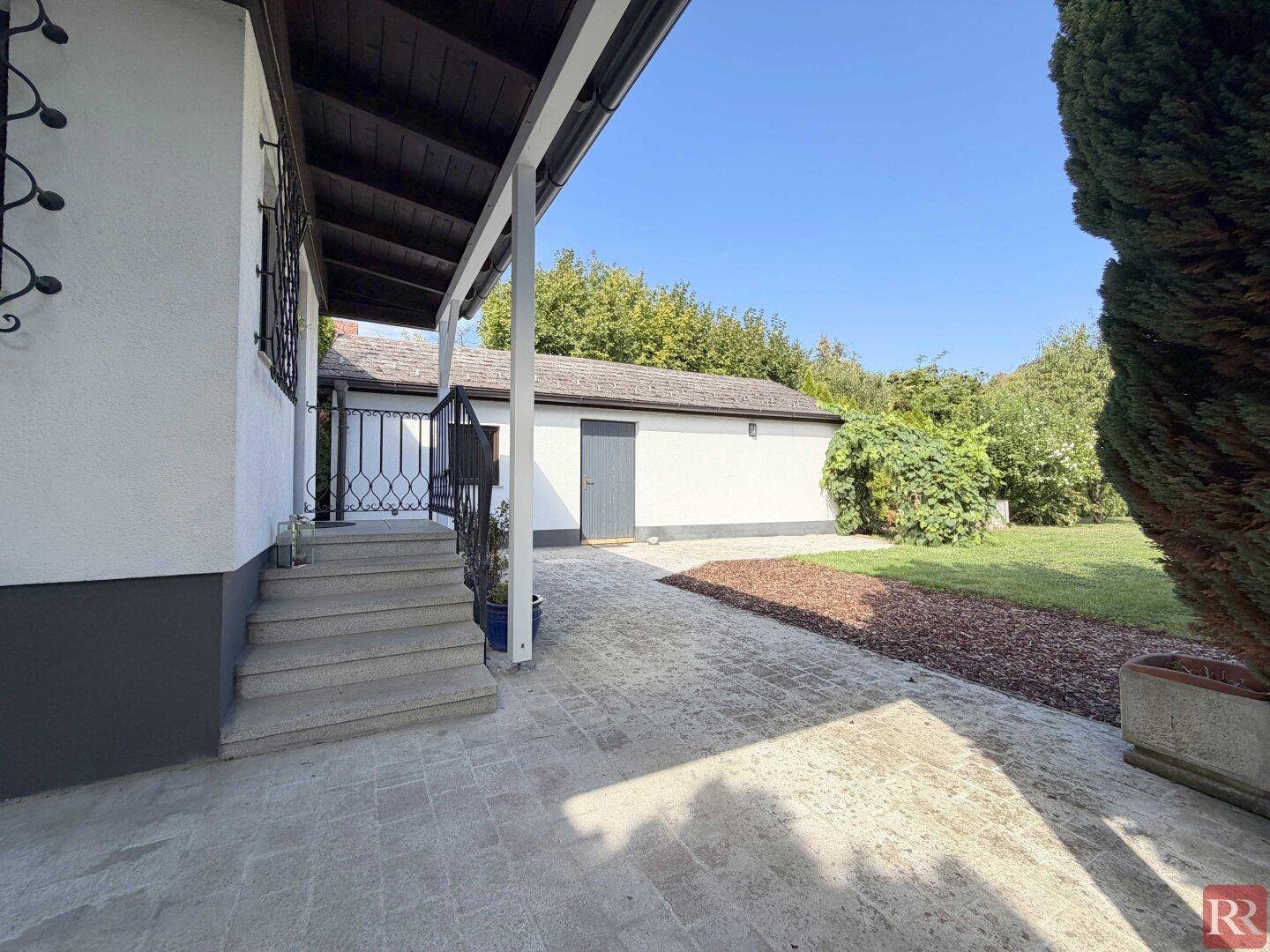Überdachter Eingangsbereich des Hauses mit Treppe und Blick auf den Garten.