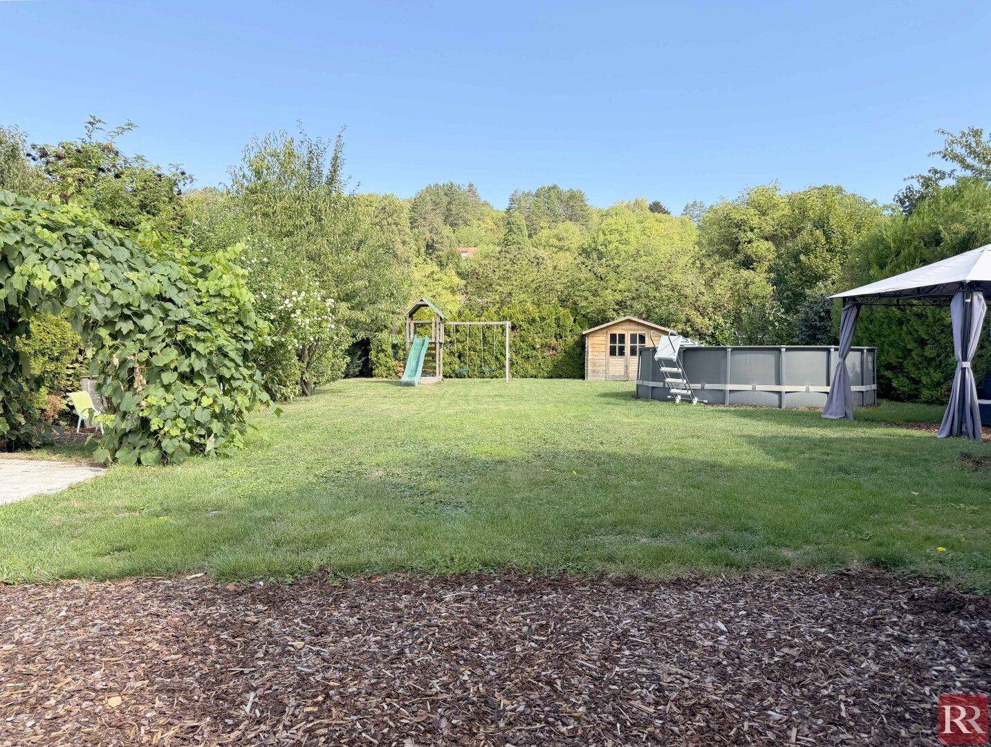 Weitläufiger Garten mit Rasen, Spielplatz, Gartenhaus und Aufstellpool.