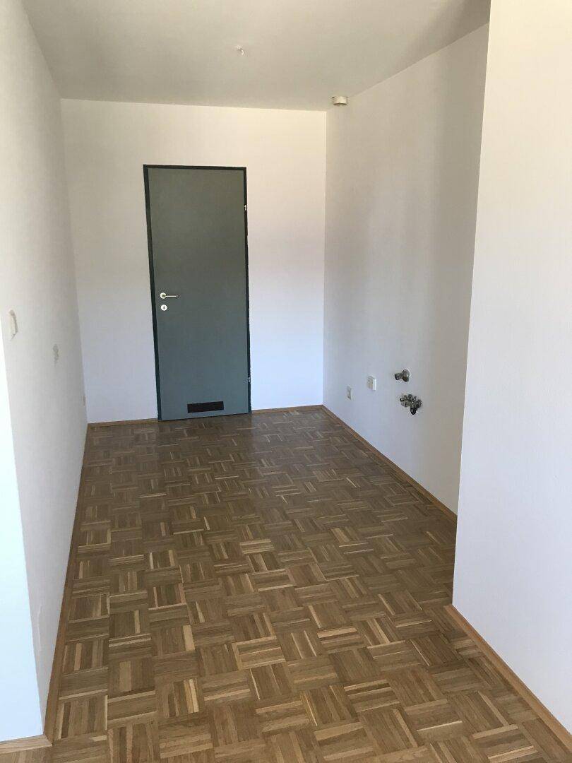 Heller Eingangsbereich mit Parkettboden, weiß gestrichenen Wänden und einer modernen Eingangstür.