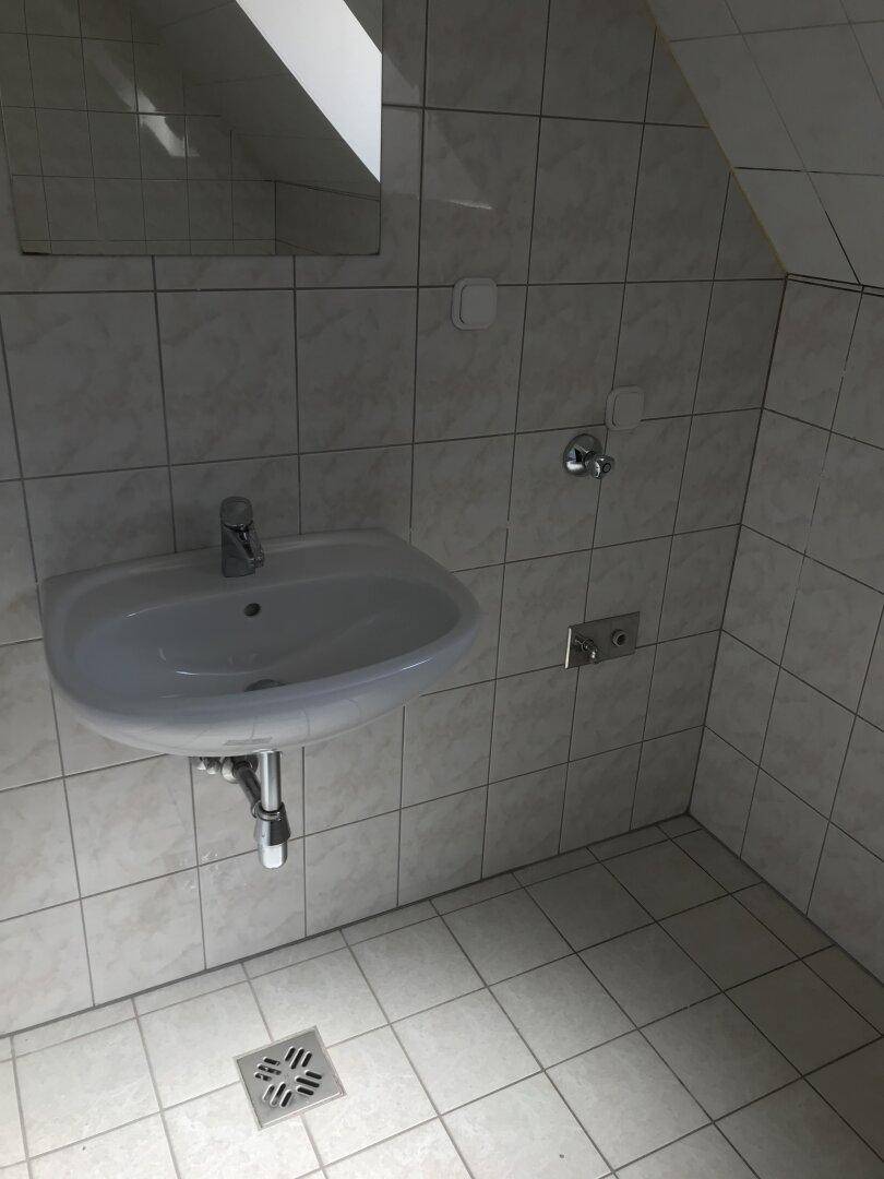 Helles Badezimmer mit weißen Fliesen, Waschbecken und Dachschräge, in gutem Zustand.