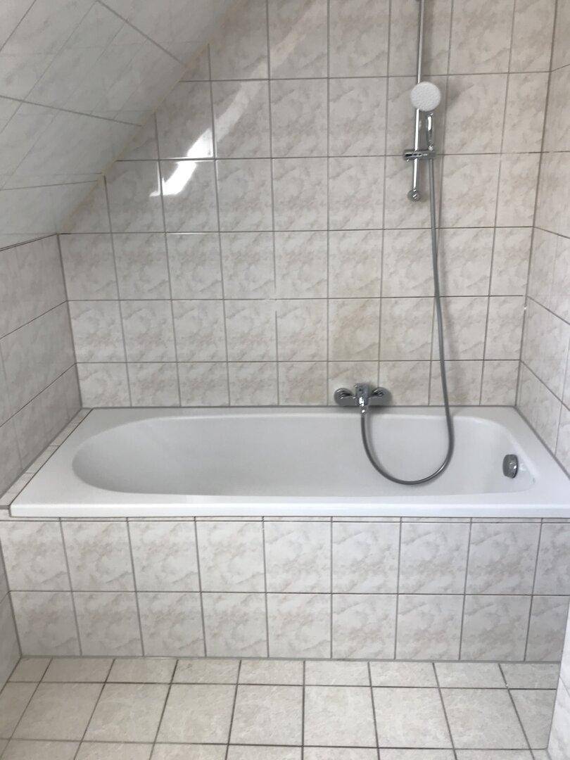 Badezimmer mit weißen Fliesen, einer Badewanne mit Duschfunktion und Dachschräge.