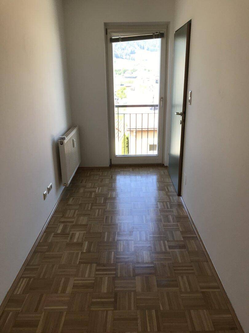 Schmaler Flur mit Parkettboden, Heizkörper und einer Tür, die zu einem französischen Balkon führt.