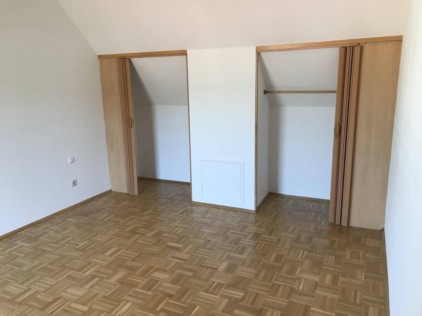 Helles Schlafzimmer mit Parkettboden, Dachschrägen und praktischen Einbauschränken.