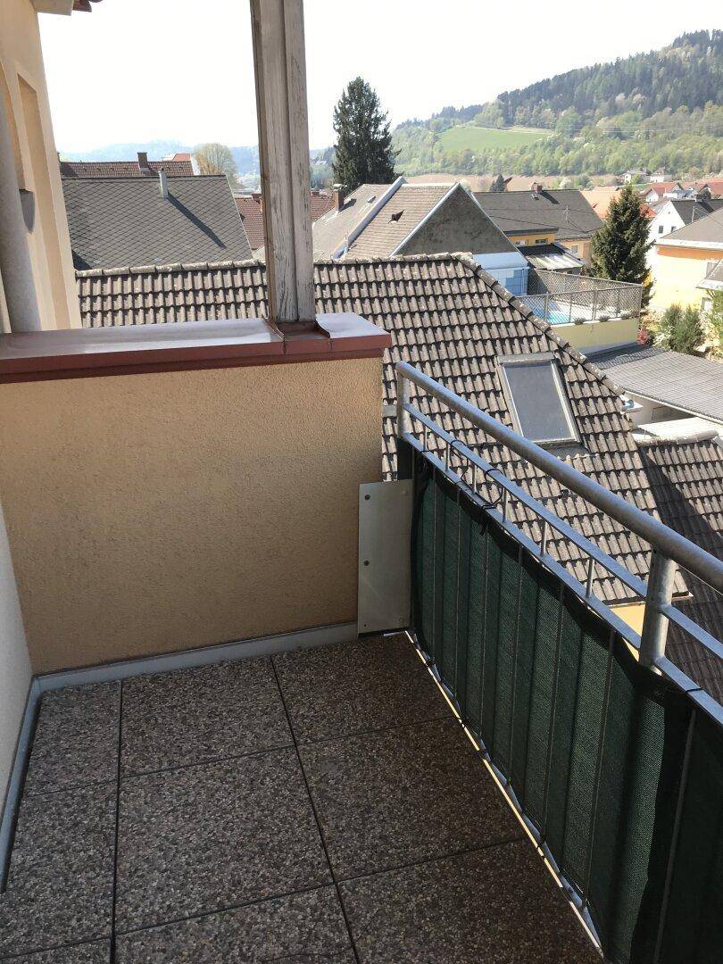 Gefliester Balkon mit Blick über Dächer, grüne Hügel und einen entfernten Poolbereich.