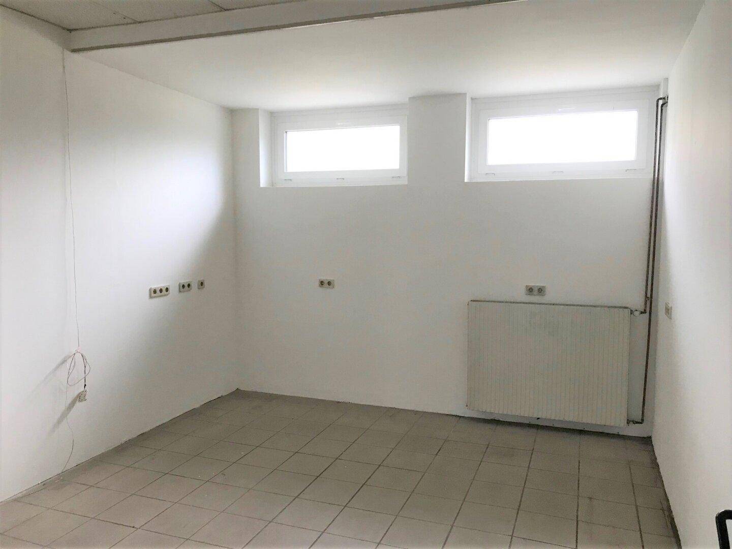 Kleinerer Raum mit zwei Fenstern, Heizkörper und Fliesenboden, ideal für Büro oder Lager.