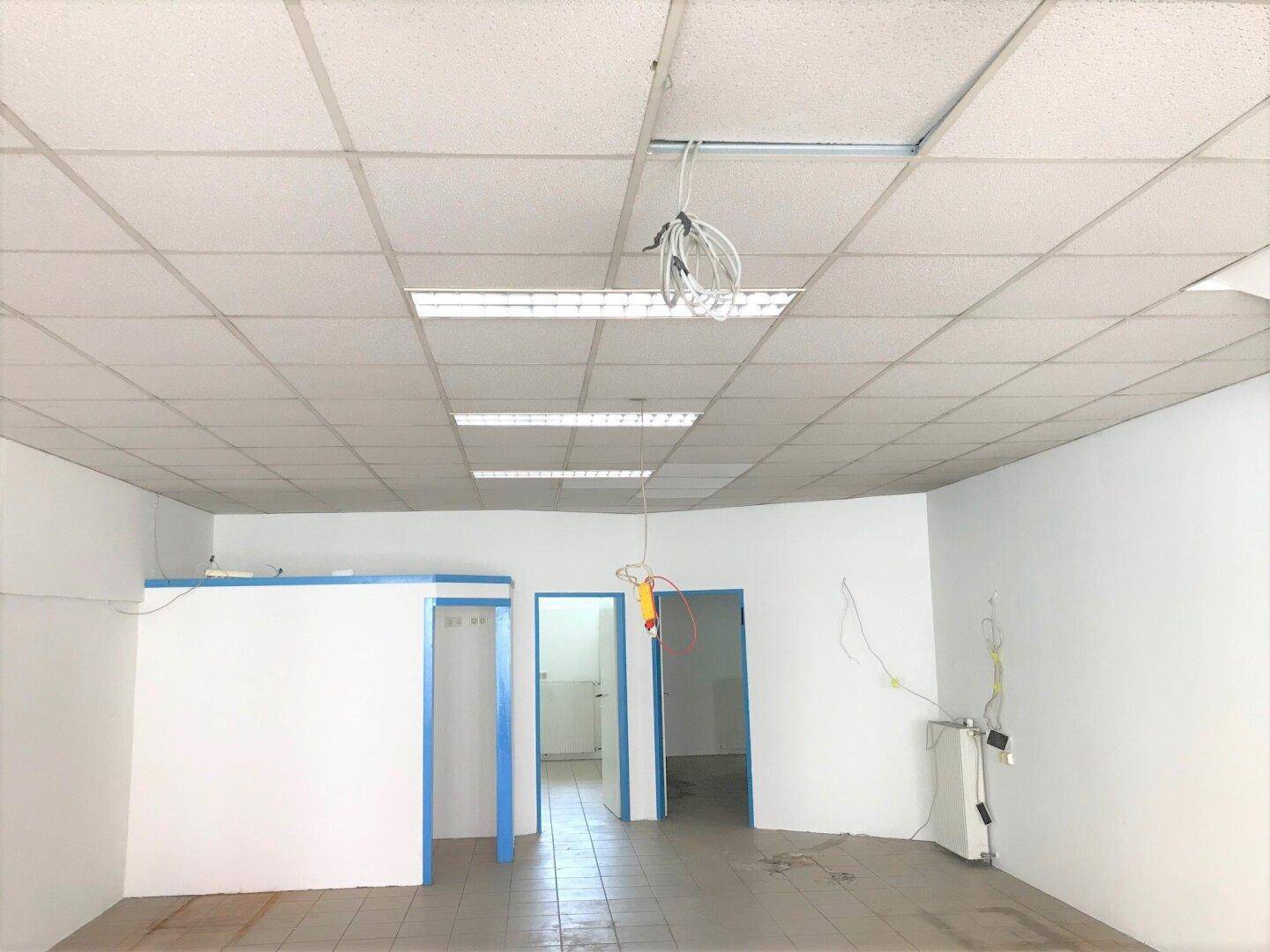 Großer, leerer Raum mit abgehängter Decke, Fliesenboden und blauen Türrahmen, bereit für den Ausbau.
