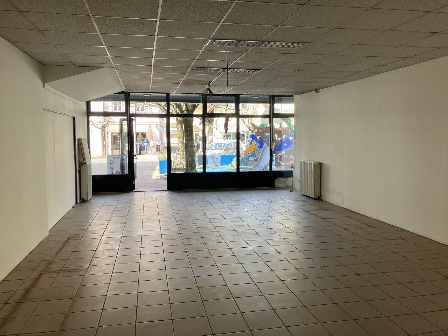Geräumiger, leerer Gewerberaum mit Fliesenboden und großen Fenstern zur Straße hin.