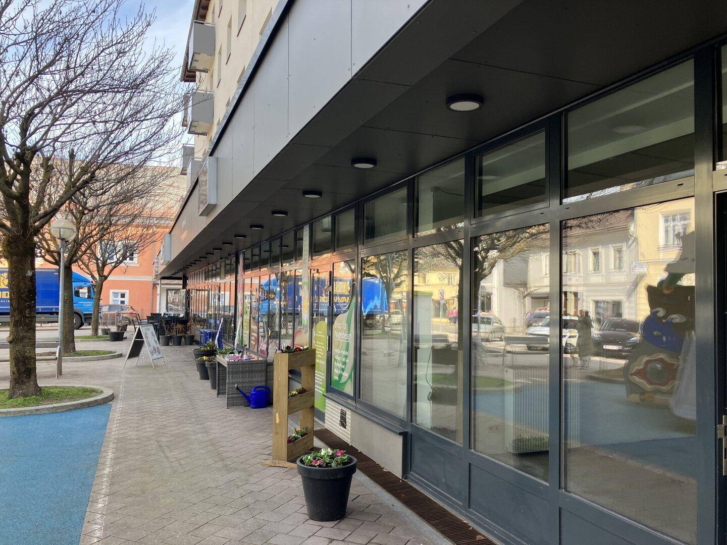 Moderne Geschäftsfassade mit großen Schaufenstern und einem Gehweg davor, der zum Eingang führt.